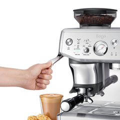 Sage espresso machine with a hand holding a spoon, a glass of coffee, and cookies on a white background